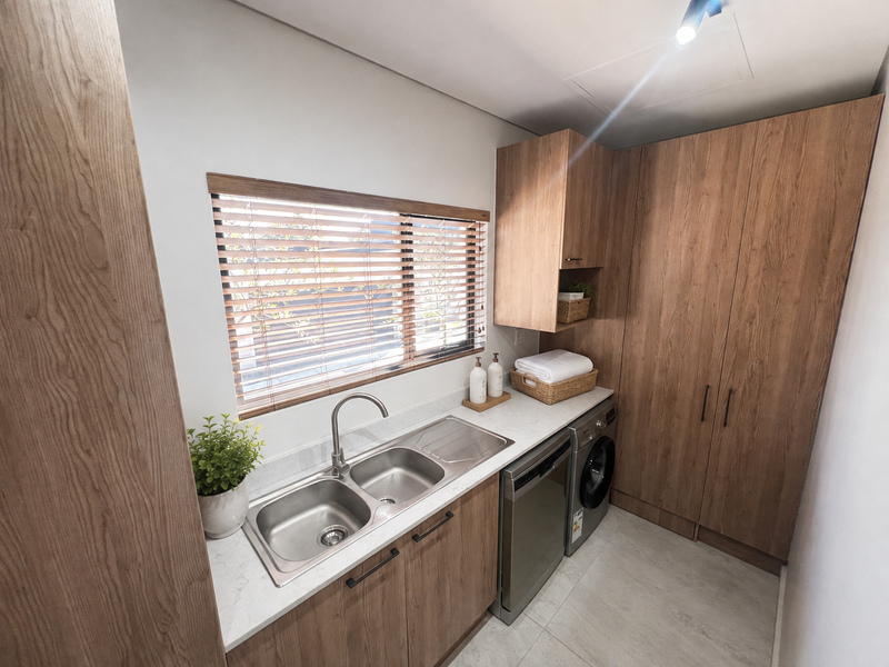 Modern laundry room featuring wood-finish cabinetry, stone countertops, a double stainless steel sink, and integrated appliances for a clean, functional workspace.