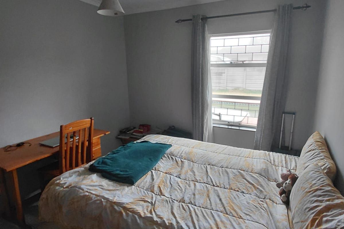 A functional bedroom featuring tiled flooring, a single pendant light fixture, and a window with curtain rod hardware.