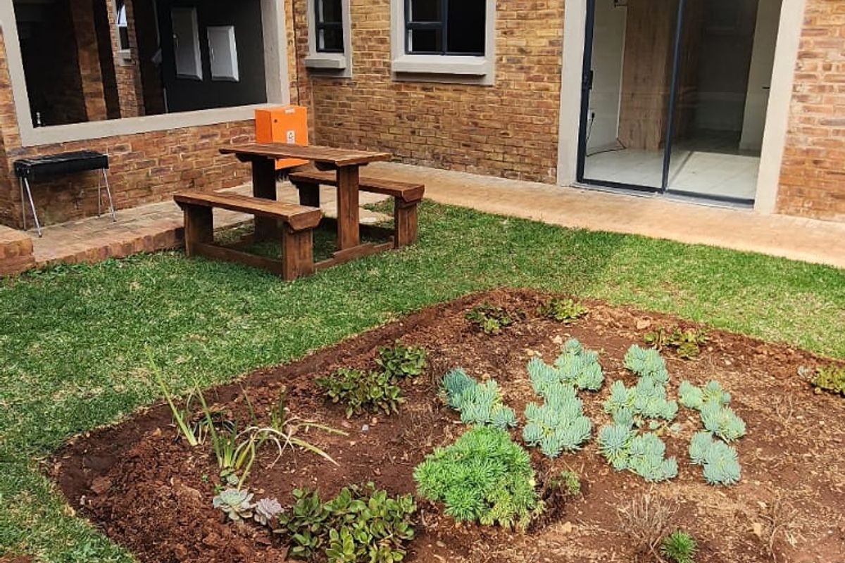 A private ground-floor garden area featuring a landscaped succulent bed, paved walkway, and direct access to the apartment interior via sliding glass doors.