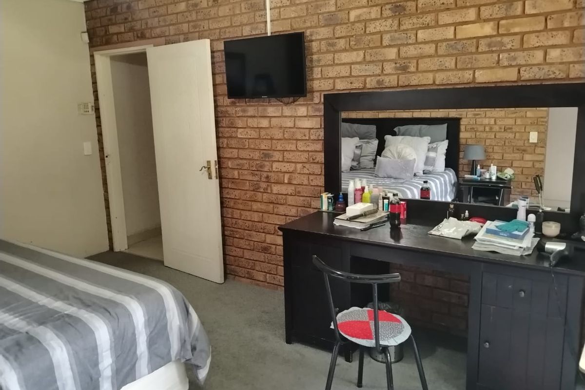A bedroom featuring a prominent exposed brick feature wall, carpeted flooring, and a doorway leading to an adjacent space.
