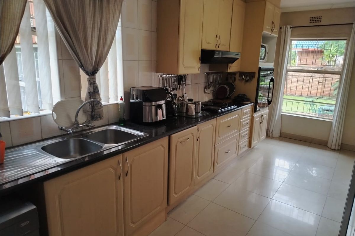 A functional kitchen featuring light-toned cabinetry, dark granite countertops, a double stainless steel sink, and built-in oven with extractor fan.