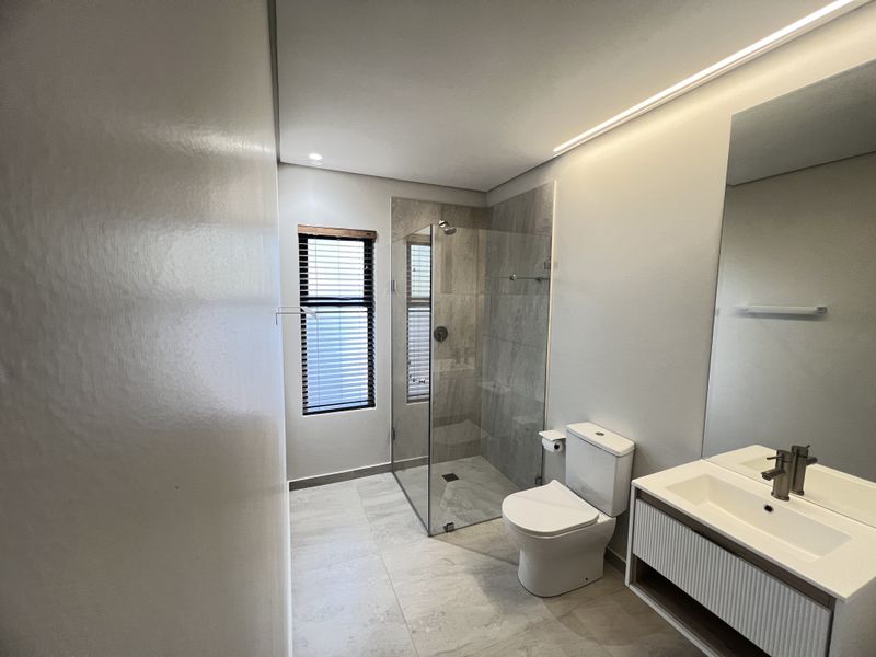 Modern, well-appointed bathroom featuring a glass-enclosed shower, contemporary wall-mounted vanity with integrated basin, and neutral floor-to-ceiling tiling.