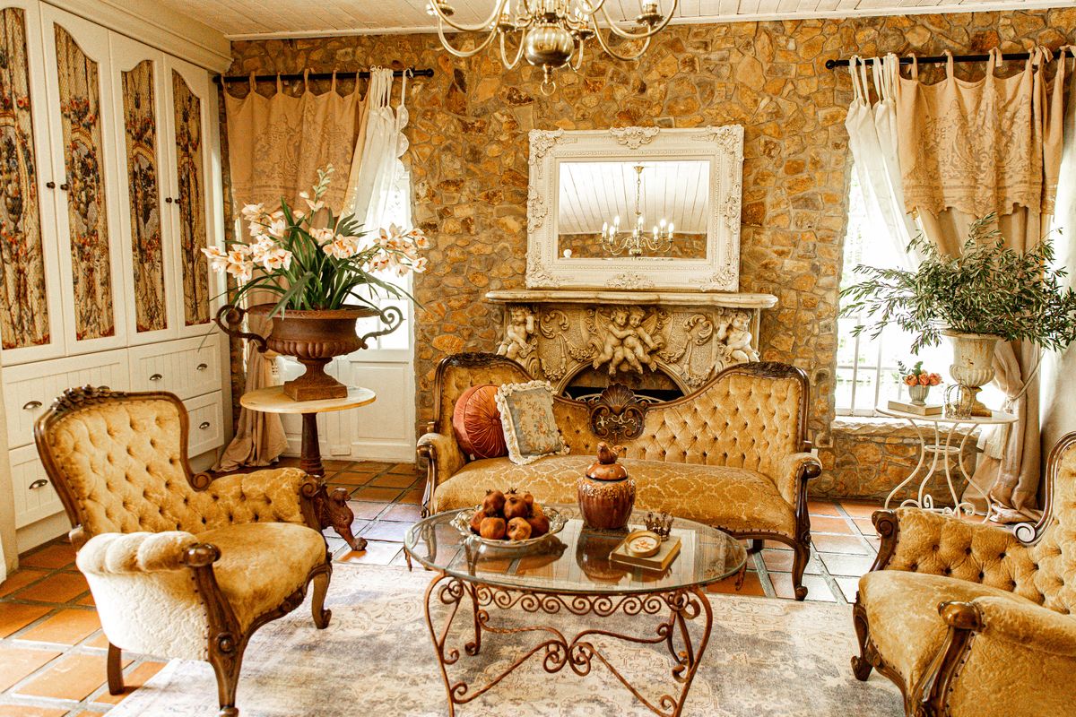 A classic living room featuring a prominent stone wall, an ornate fireplace mantel, built-in cabinetry, and traditional terracotta floor tiles.