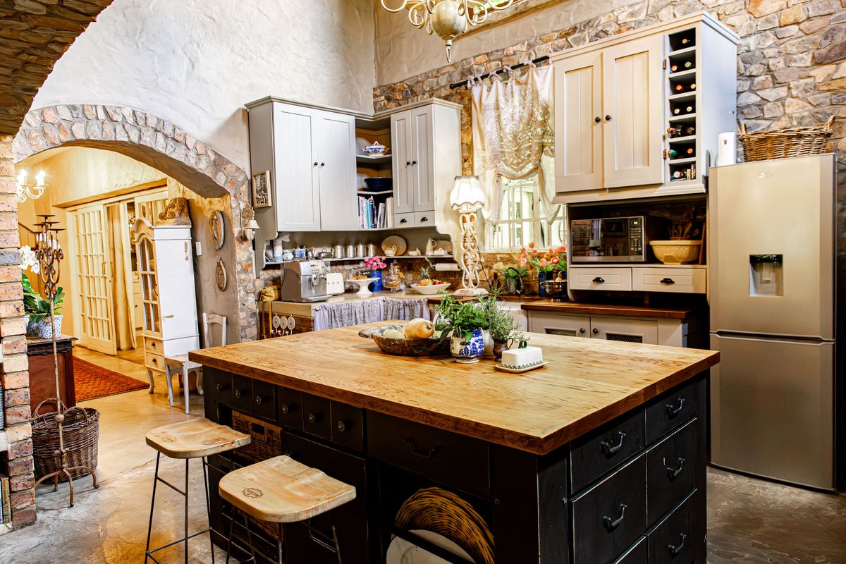 A rustic-style kitchen featuring a large wooden island, stone feature walls, an arched entryway, and custom cabinetry with integrated appliances.