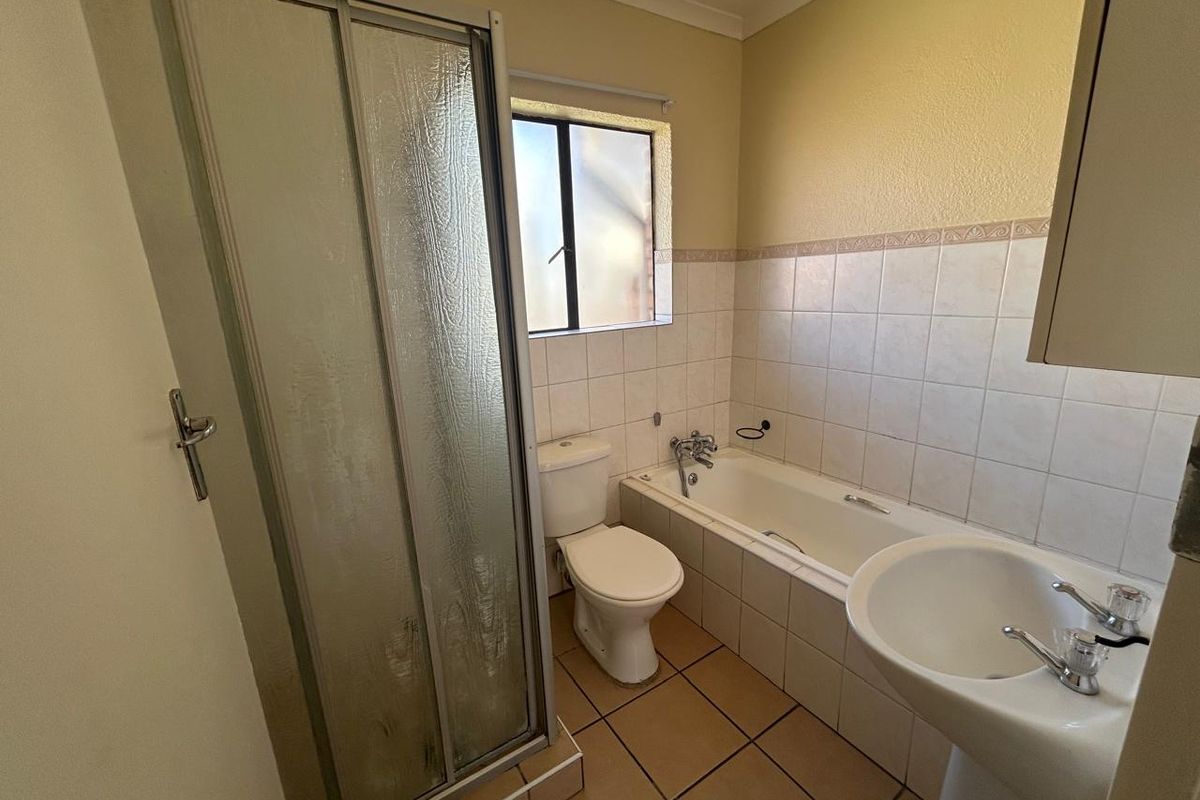 A functional bathroom featuring a shower enclosure, bathtub, pedestal basin, and toilet with neutral wall and floor tiling.