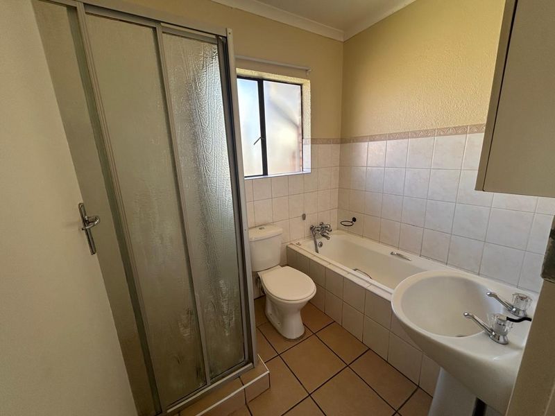 A functional bathroom featuring a shower enclosure, bathtub, pedestal basin, and toilet with neutral wall and floor tiling.