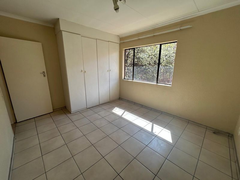 An empty bedroom featuring tiled flooring, built-in cupboards, and a window with natural light, offering a blank canvas for potential interior updates.