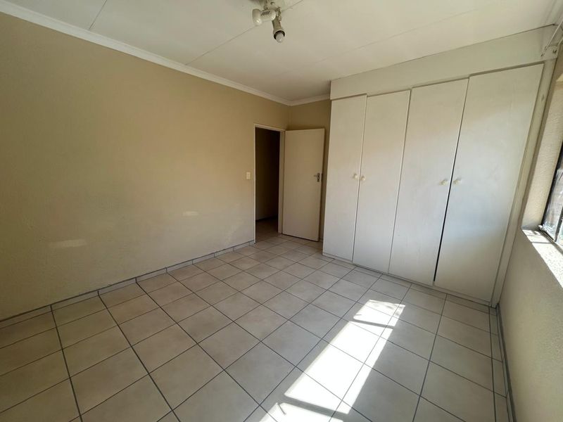 An empty bedroom featuring tiled flooring and built-in cupboards, offering a blank canvas for personalization.