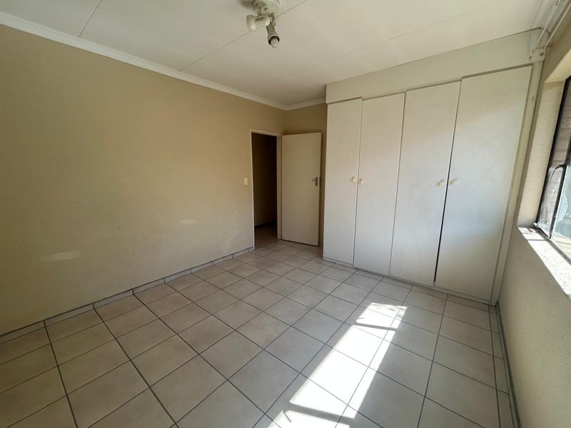 An empty bedroom featuring tiled flooring and built-in cupboards, offering a blank canvas for personalization.