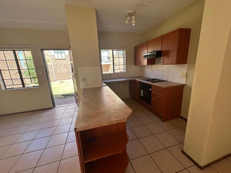 Open plan kitchen featuring wooden cabinetry, laminate countertops, built-in oven and hob, with direct access to the rear garden area.