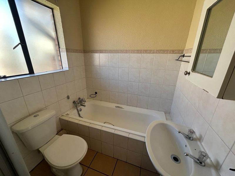 A functional bathroom featuring a bathtub, pedestal basin, and toilet, finished with neutral wall and floor tiles.