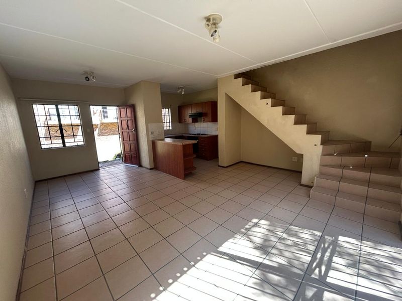 Open-plan living area featuring tiled flooring, a functional kitchen with built-in cabinetry, and a staircase leading to the upper level.