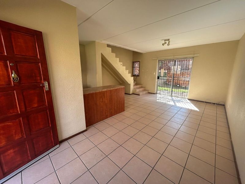 Open-plan living area featuring tiled flooring, a built-in staircase, and a sliding door leading to the exterior, offering a blank canvas for interior design.