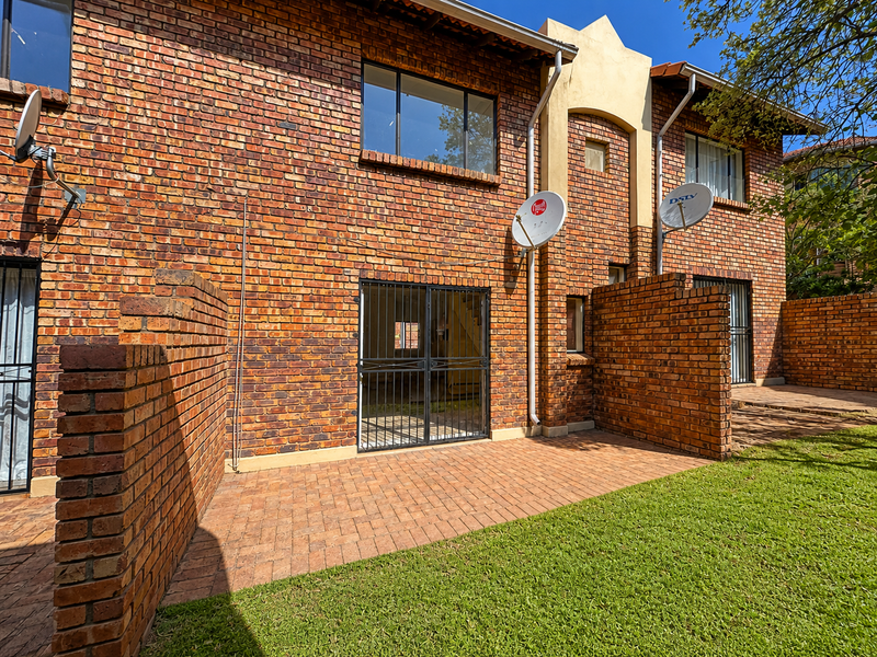 Rear view of a townhouse featuring a face brick facade, paved patio area, and a private lawn.