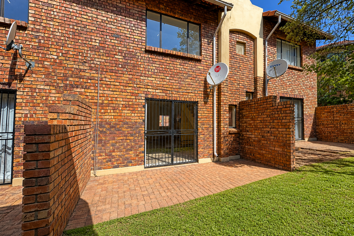 Rear view of a townhouse featuring a face brick facade, paved patio area, and a private lawn.