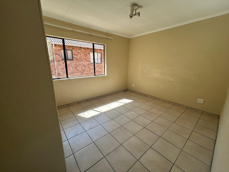 An empty bedroom featuring tiled flooring, a built-in cupboard, and a metal-framed window, offering a blank canvas for personalization and renovation.