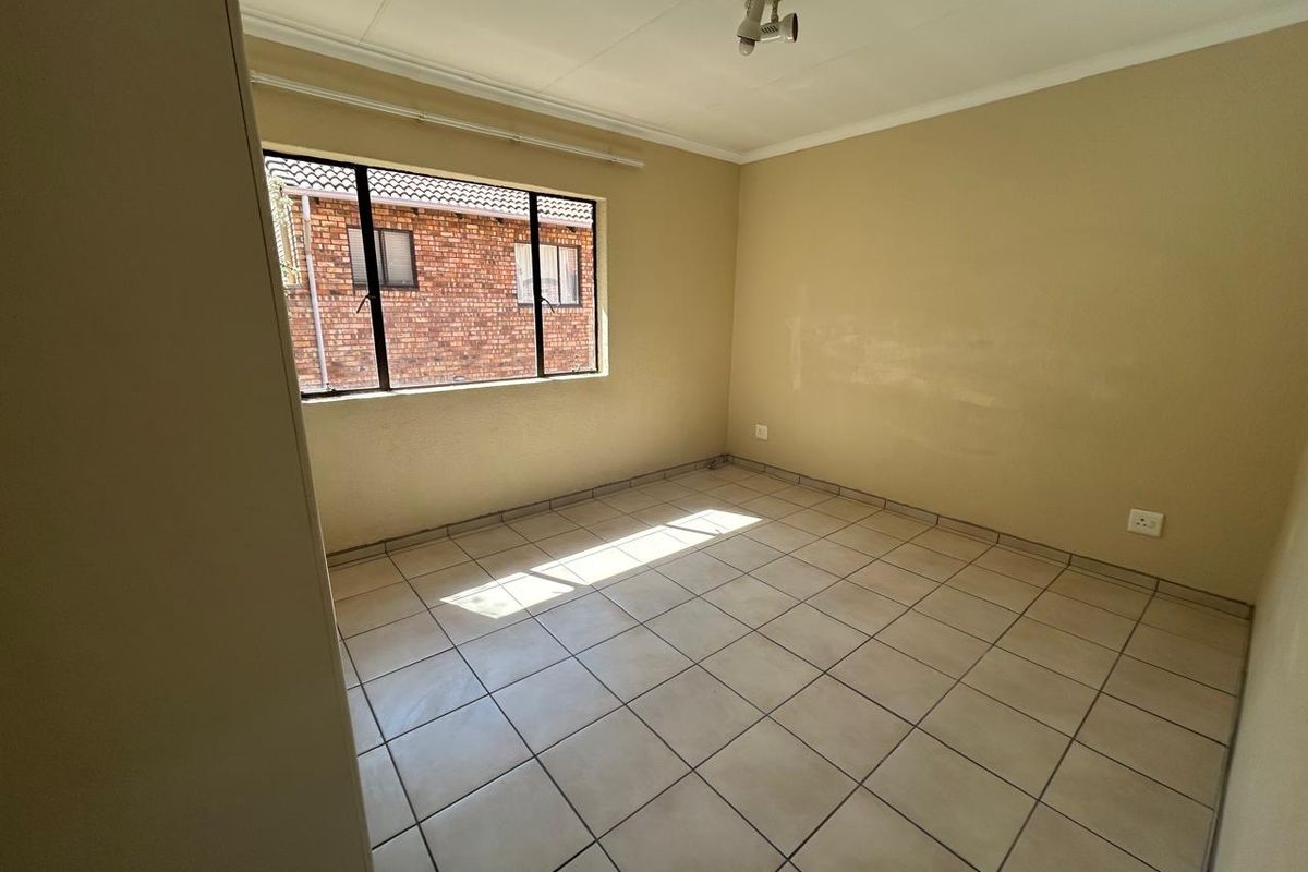An empty bedroom featuring tiled flooring, a built-in cupboard, and a metal-framed window, offering a blank canvas for personalization and renovation.
