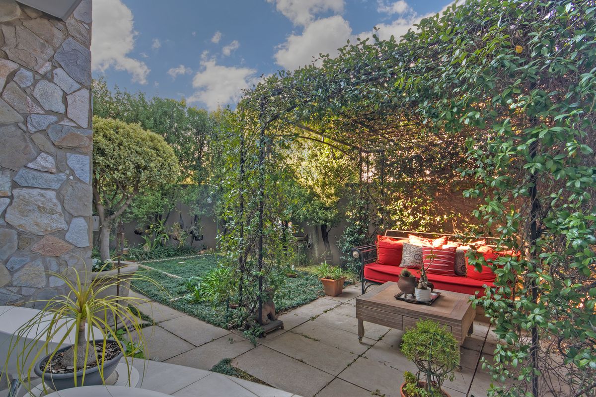 A private rear garden featuring a paved patio area, a metal pergola covered in climbing vines, and established landscaping.