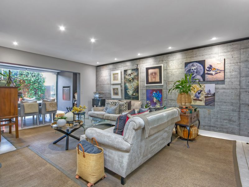 Spacious living room featuring a striking exposed concrete feature wall, recessed downlighting, and seamless flow to an adjoining outdoor patio area.