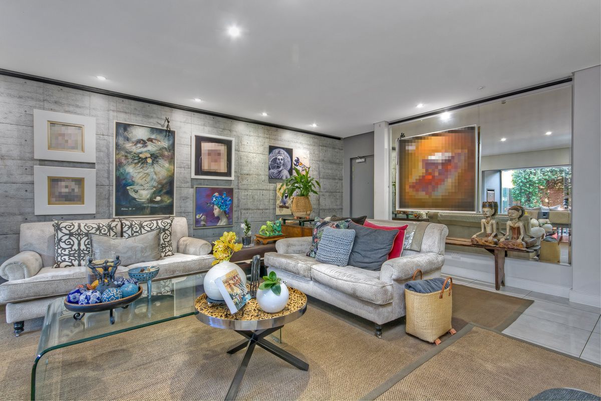 A well-maintained living room featuring a striking concrete feature wall, recessed downlighting, and a large mirrored wall panel that enhances the sense of space.