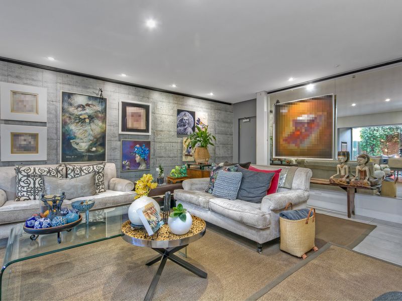 A well-maintained living room featuring a striking concrete feature wall, recessed downlighting, and a large mirrored wall panel that enhances the sense of space.
