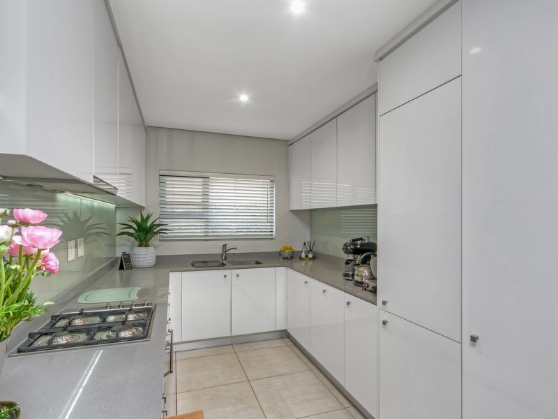Modern kitchen featuring high-gloss white cabinetry, stone countertops, a gas hob, integrated appliances, and a glass splashback with ample storage space.