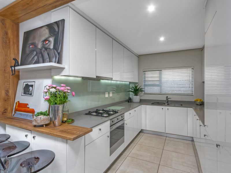 Modern kitchen featuring high-gloss white cabinetry, stone countertops, integrated gas hob, built-in oven, and a sleek glass splashback with recessed lighting.