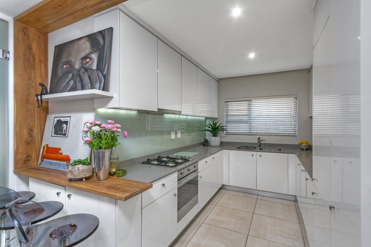 Modern kitchen featuring high-gloss white cabinetry, stone countertops, integrated gas hob, built-in oven, and a sleek glass splashback with recessed lighting.