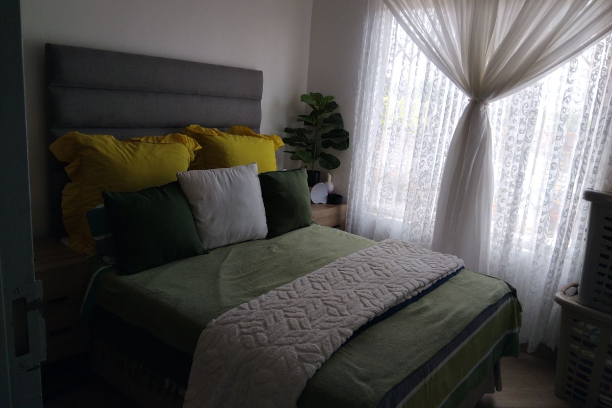 A cozy bedroom featuring tiled flooring and a window fitted with a security gate, allowing for natural light.