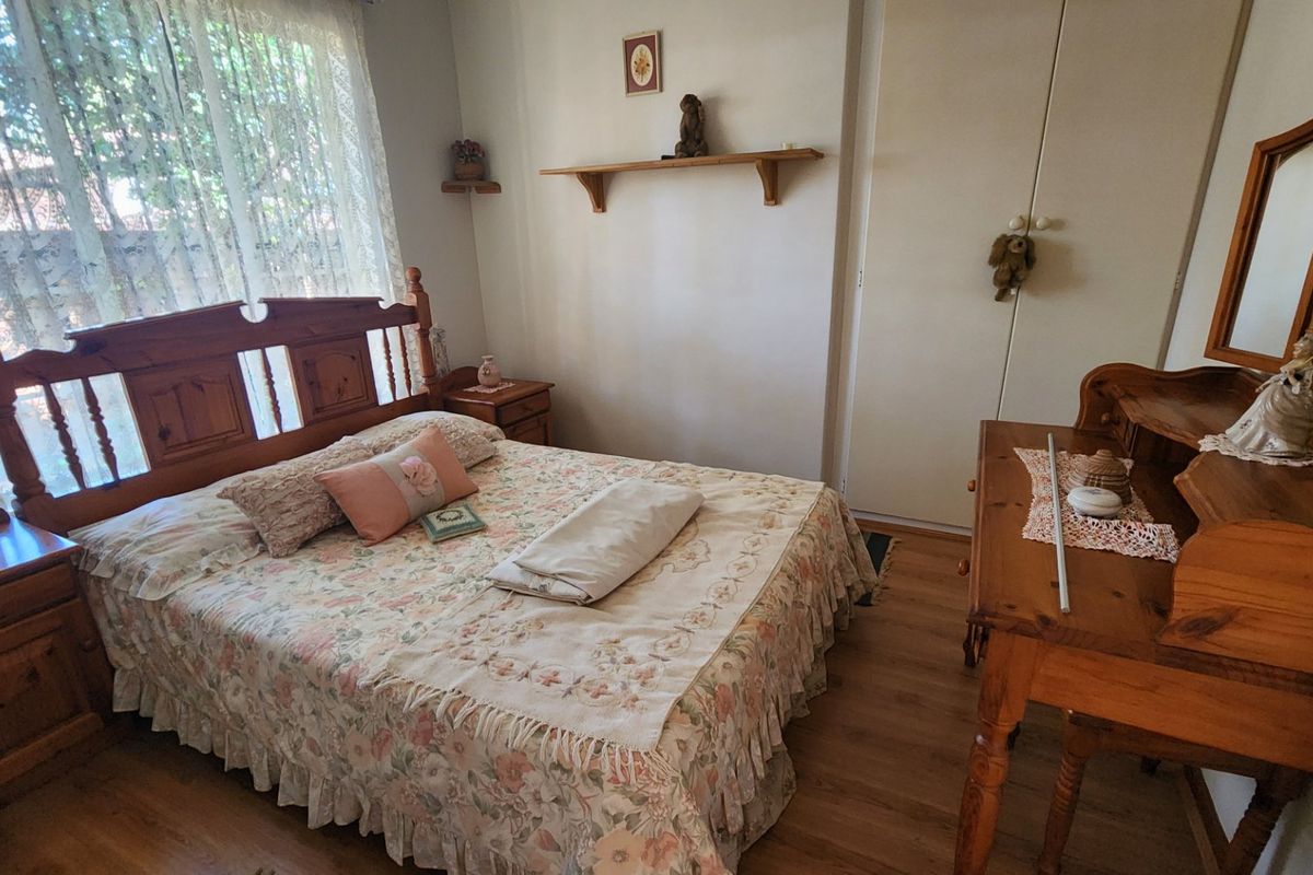 A cozy bedroom featuring wood-look flooring, built-in wardrobe storage, and a window with sheer curtains.