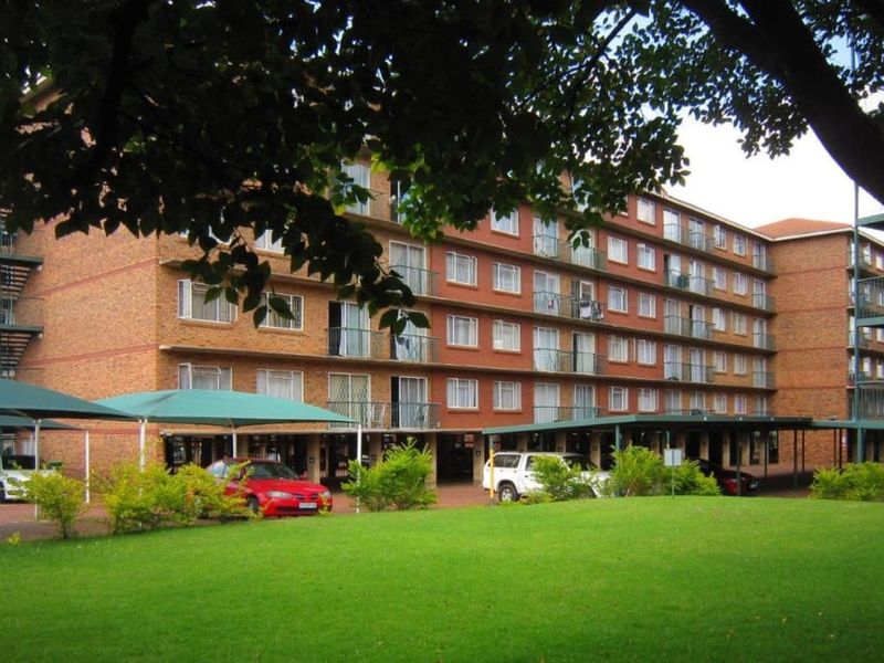 Exterior view of a multi-story brick apartment complex featuring covered parking bays, external staircases, and private balconies for each unit.