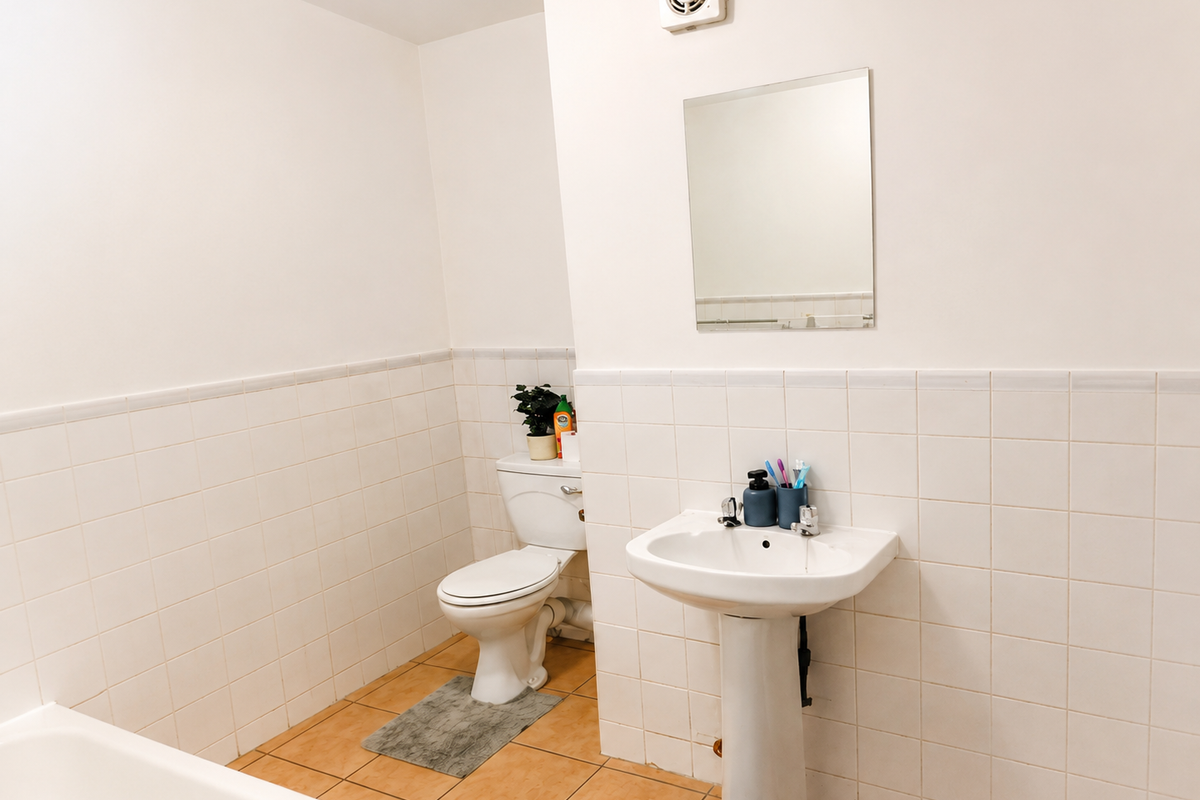 A functional bathroom featuring a pedestal sink, toilet, wall-mounted mirror, and extractor fan, finished with neutral ceramic wall and floor tiles.