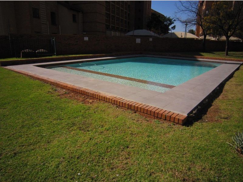 A well-maintained outdoor swimming pool area featuring a paved surround, brick coping, and a surrounding perimeter wall within a landscaped garden setting.