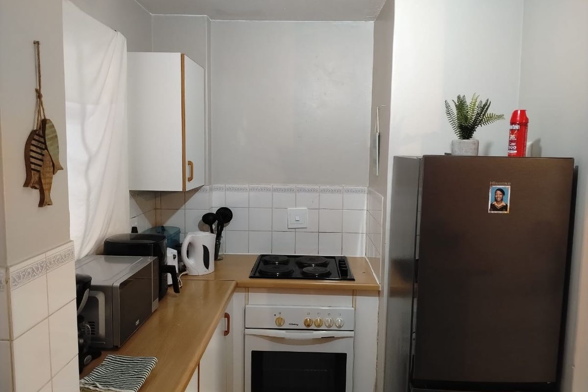 A compact kitchen featuring a built-in oven, electric hob, laminate countertops, and tiled backsplash with overhead cabinetry.