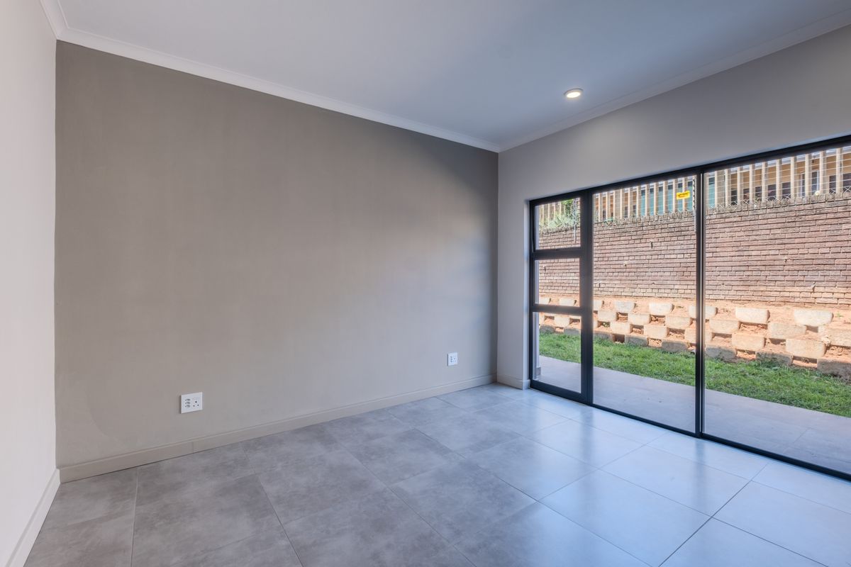 A bright, empty living area featuring modern grey floor tiles, neutral walls, and a large sliding glass door providing access to the outdoor space.