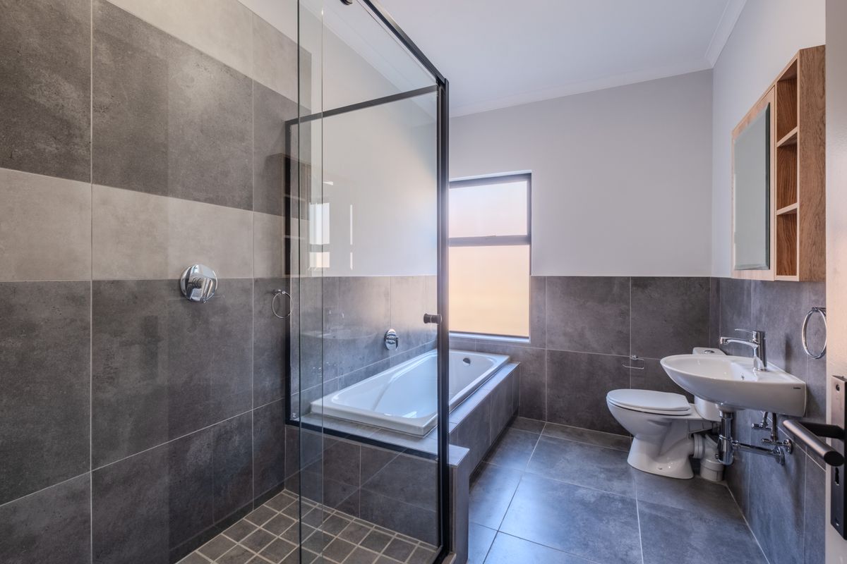 Modern bathroom featuring a built-in bathtub, glass-enclosed shower, pedestal washbasin, and contemporary grey tiling throughout.