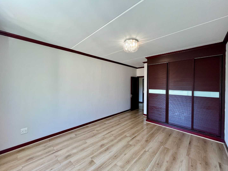 A bright, empty bedroom featuring modern laminate flooring, a large built-in sliding door wardrobe, and decorative ceiling and floor trim.