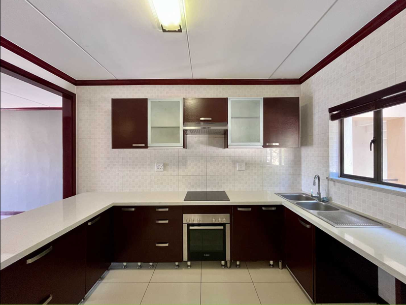 A clean, U-shaped kitchen featuring dark wood cabinetry, white quartz countertops, integrated oven and hob, and a double sink with tiled backsplash.
