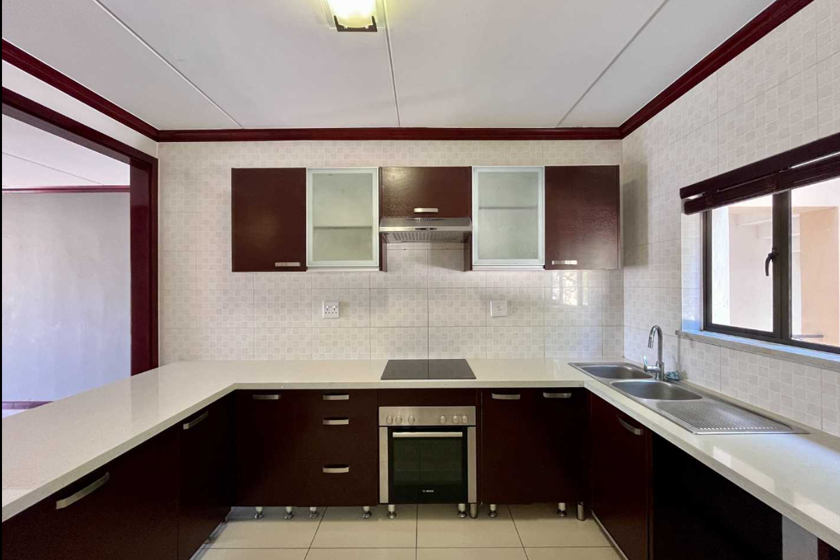 A clean, U-shaped kitchen featuring dark wood cabinetry, white quartz countertops, integrated oven and hob, and a double sink with tiled backsplash.