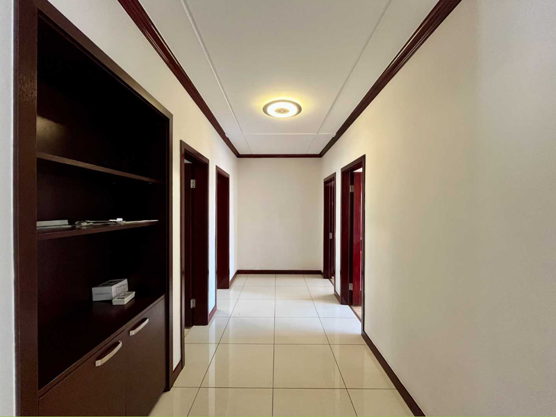 A clean and well-maintained hallway featuring tiled flooring, built-in dark wood cabinetry, and multiple doorways leading to other rooms.