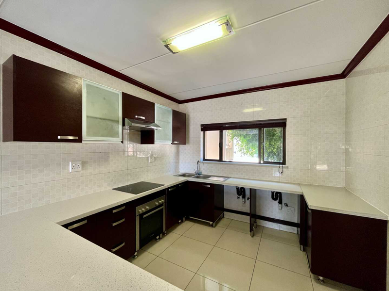 A functional kitchen featuring dark cabinetry, stone countertops, integrated oven and hob, and tiled finishes. The space is clean and ready for final touches.