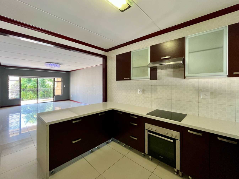 Open-plan kitchen featuring dark cabinetry, integrated appliances, and tiled flooring, flowing seamlessly into a spacious living area with access to a balcony.