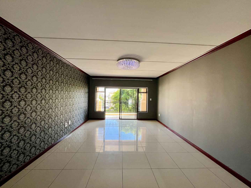 A spacious, empty living room featuring polished tile floors, decorative wallpaper, and a sliding glass door leading to an outdoor balcony.
