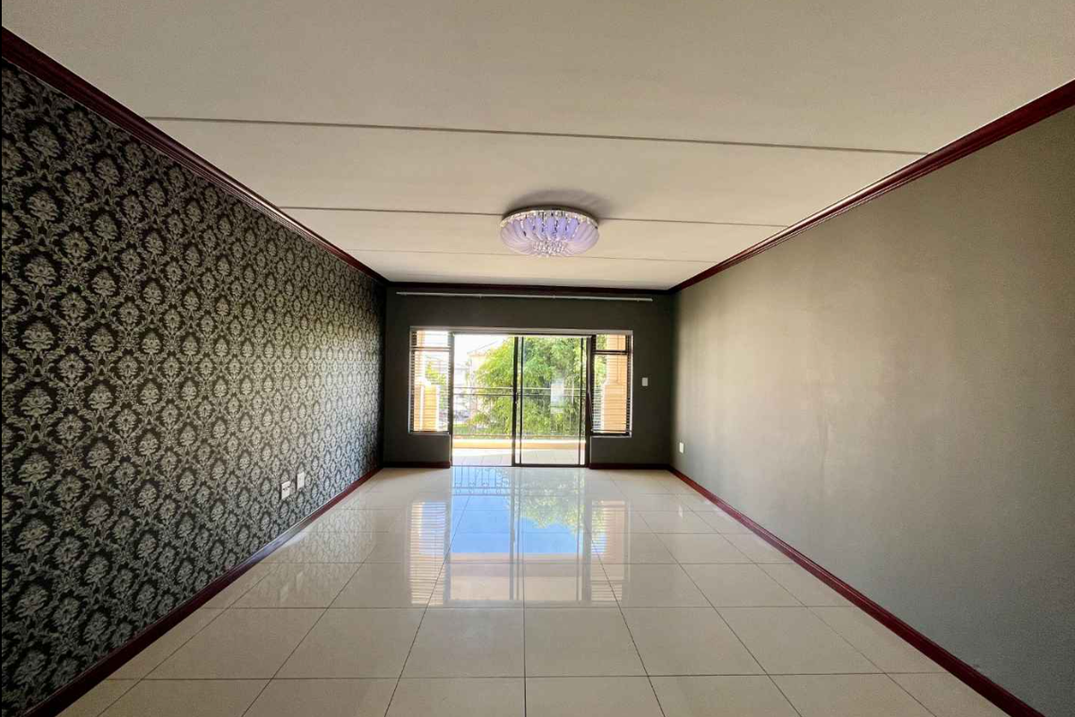A spacious, empty living room featuring polished tile floors, decorative wallpaper, and a sliding glass door leading to an outdoor balcony.