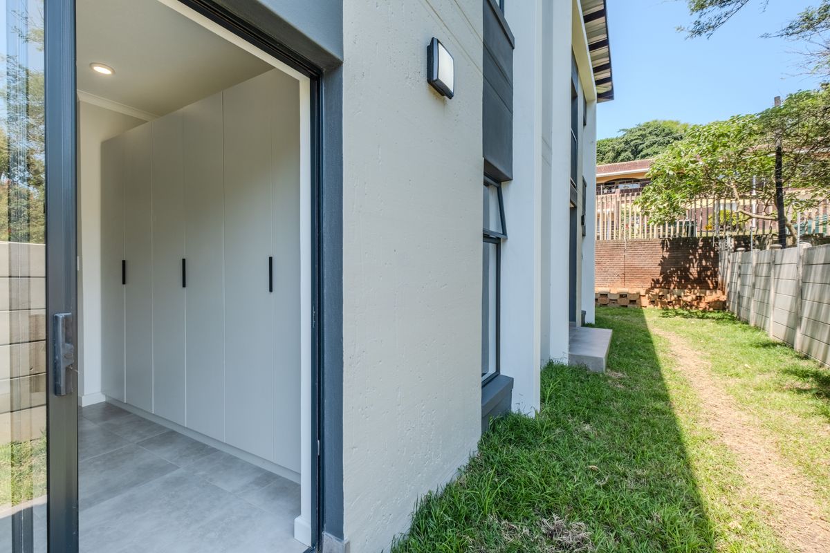 A view of the rear exterior showing a sliding door leading into a room with built-in cupboards, adjacent to a private lawn and boundary wall.