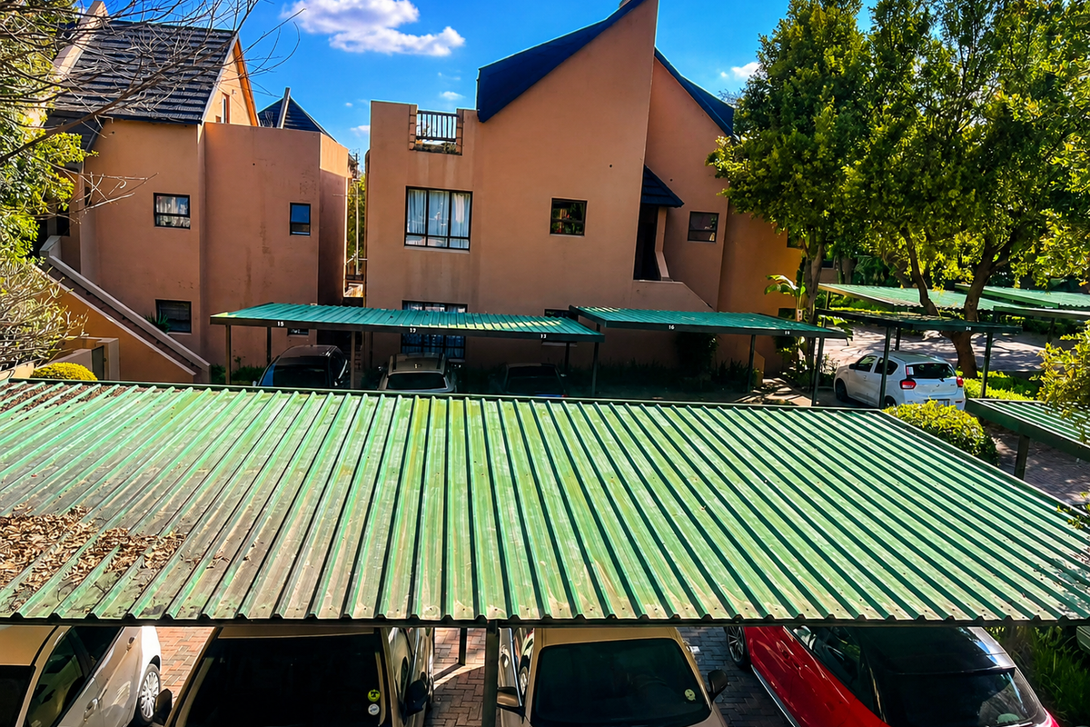 Exterior view of the apartment complex featuring covered parking bays with corrugated metal roofing and paved driveway access.