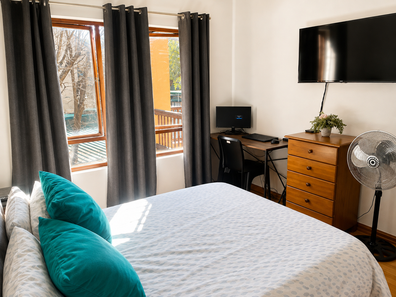 A functional bedroom featuring timber-framed windows, laminate flooring, and wall-mounted television space, offering a comfortable layout for residents.