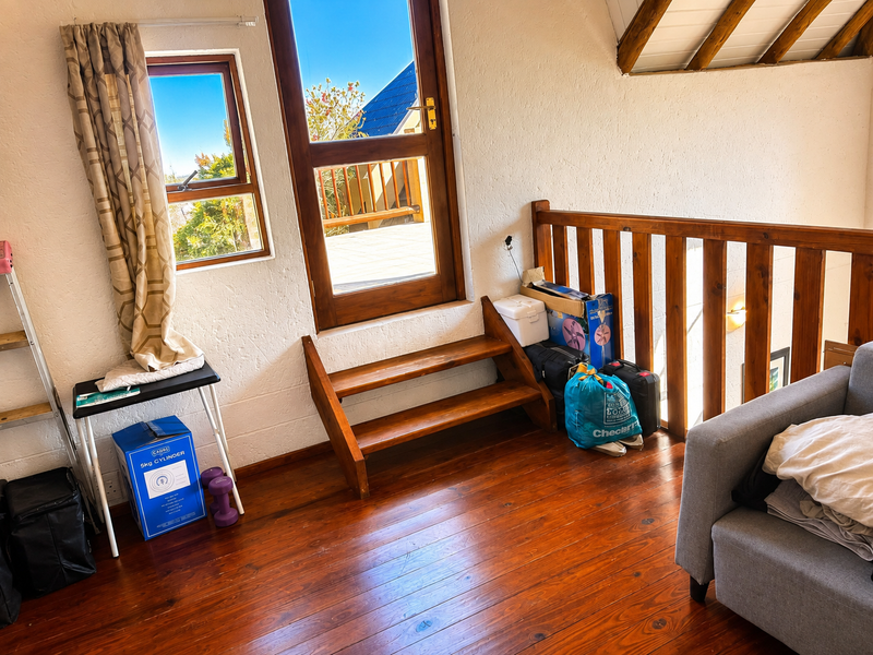 A loft-style living area featuring warm timber flooring, exposed rafters, and a wooden staircase leading to an exterior door with natural light.