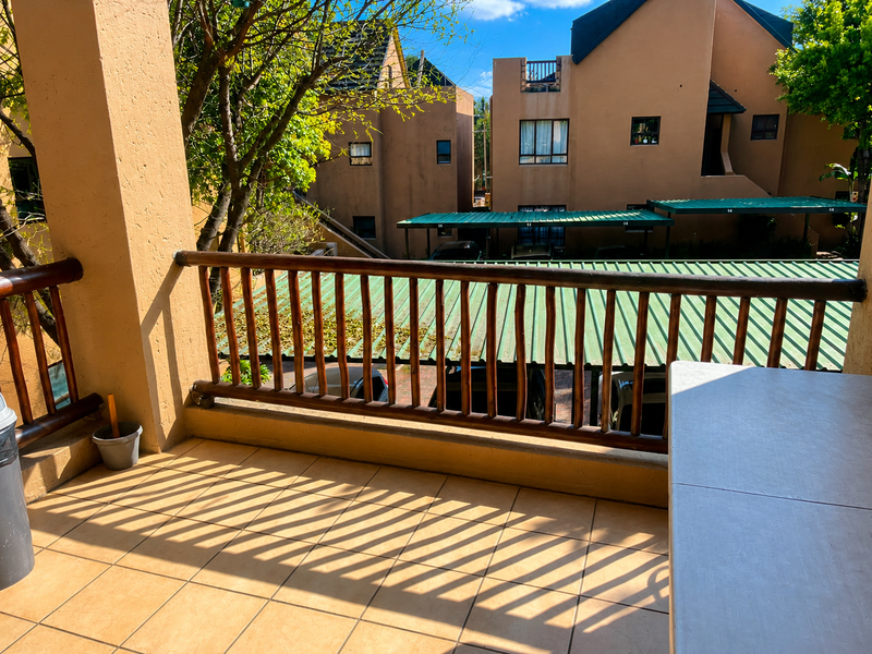 A covered balcony featuring tiled flooring and a wooden balustrade, overlooking the apartment complex parking area.