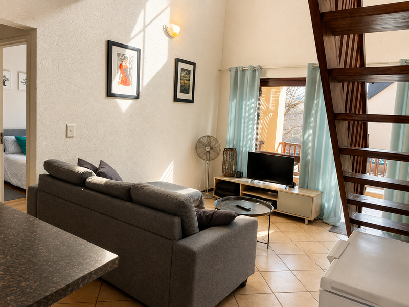 A bright living room featuring tiled flooring, a wooden staircase leading to an upper level, and direct access to an outdoor balcony area.